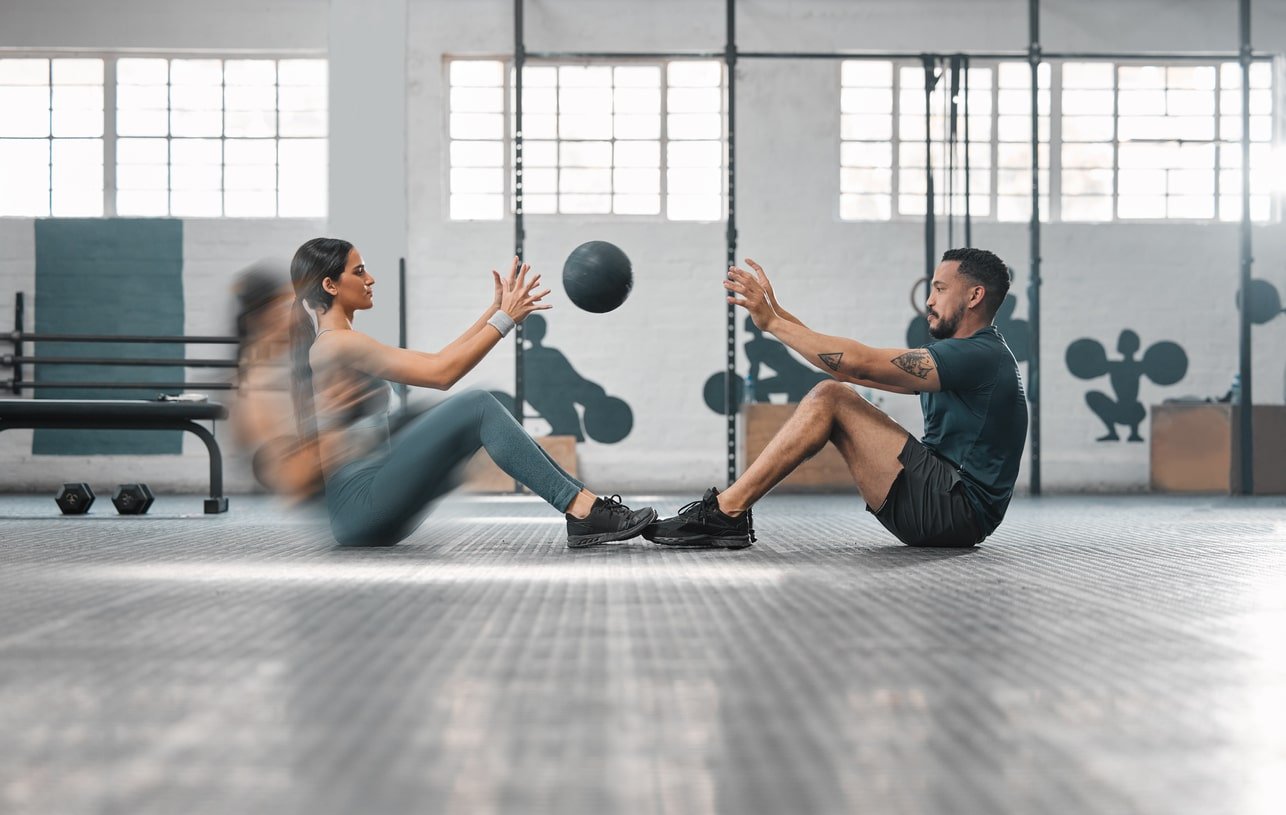 Male trainer and female athlete in motion focused on workout session with slam ball.