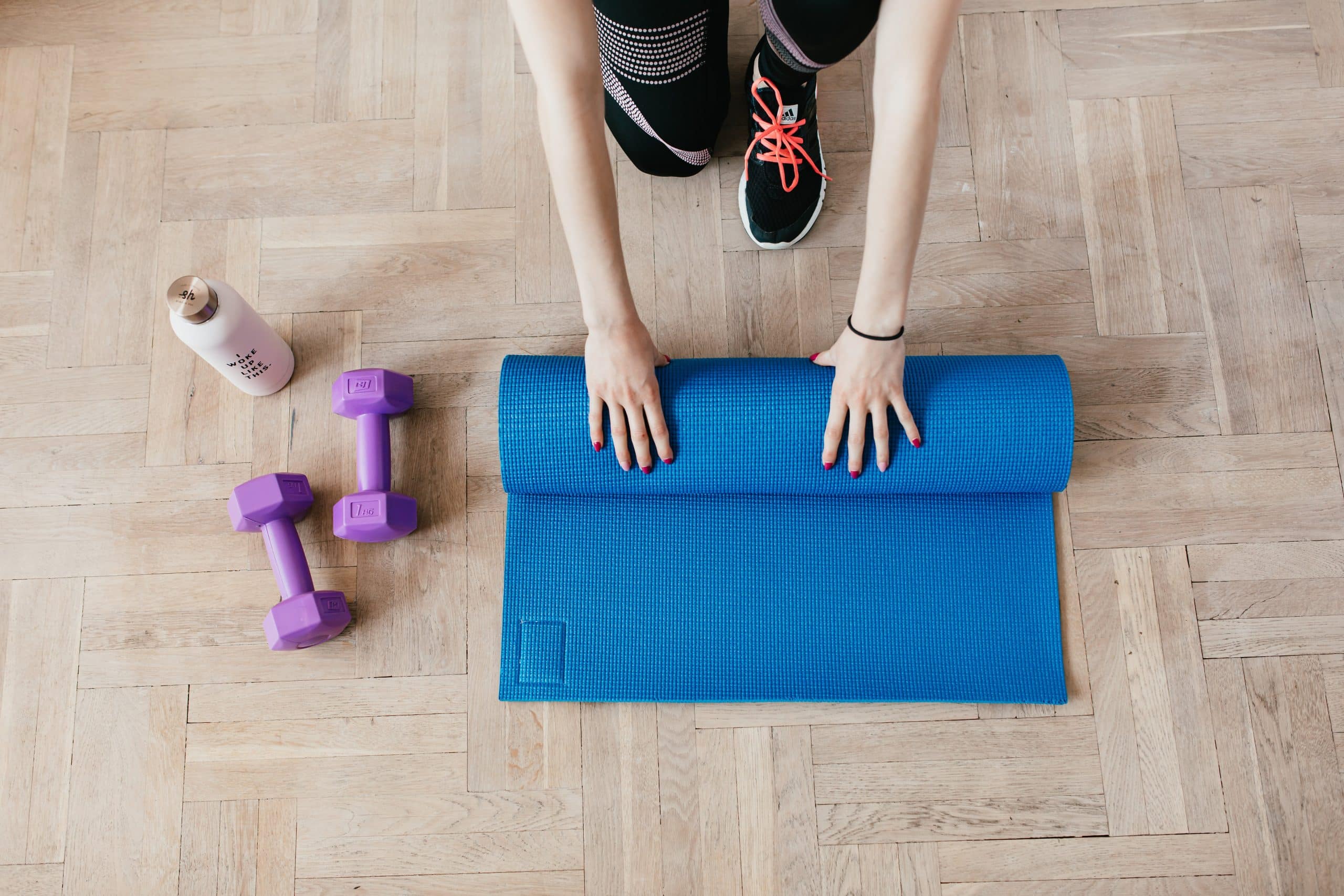 A pair of purple dumbbells next to a blue yoga mat being rolled up